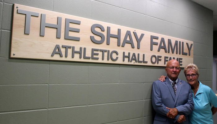 Jon and Linda Shay pose near the sign of The Shay Family Athletic Hall of Fame